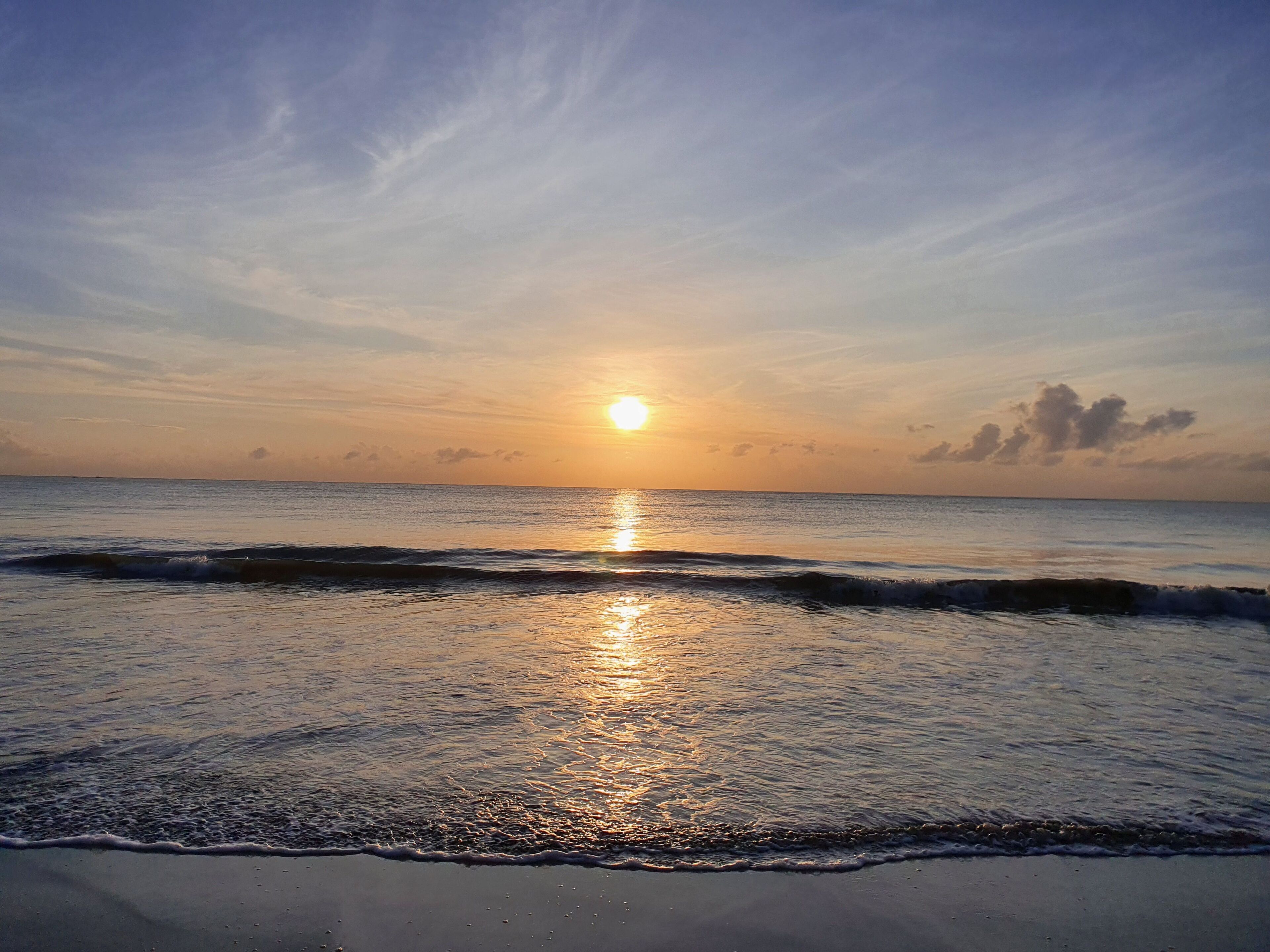 Une plage au coucher du soleil, où les vagues viennent doucement lécher le rivage.