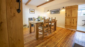 Un tavolo da pranzo in legno con sedie, una televisione e un piccolo tavolo con bottiglie di vino e bicchieri. Alle pareti sono appese delle foto incorniciate e una porta in legno con una maniglia.