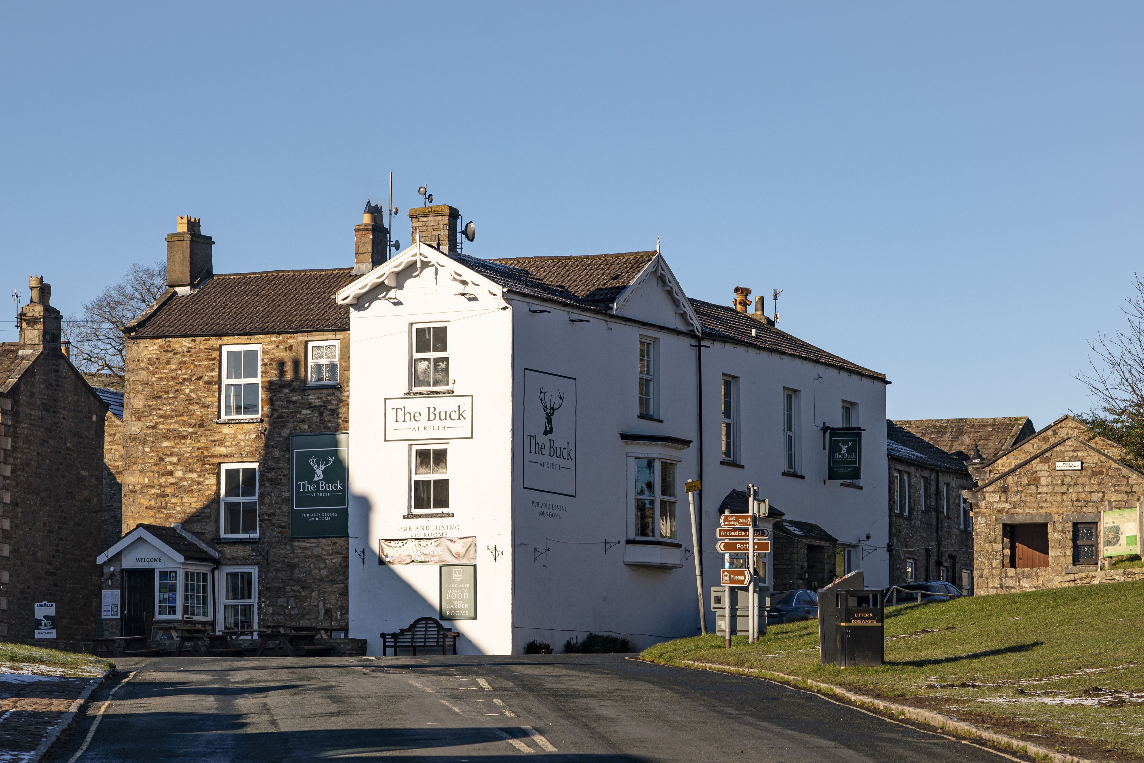 A traditional pub named "The Buck" with a signboard, a welcoming entrance, and a visible seating area outside.
