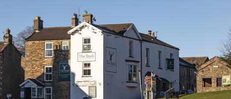 A traditional pub named "The Buck" with a signboard, a welcoming entrance, and a visible seating area outside.