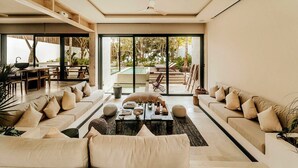A spacious living area with a large sofa set, a coffee table, and a pool visible through the glass doors. - Azumaya Beach House Tulum – Beachfront, Chef Included (Tulum)