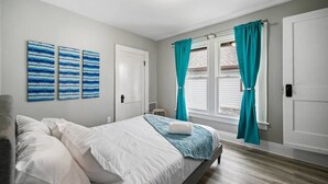 Ein Schlafzimmer mit einem Bett, einem Nachttisch, einem Fenster mit Vorhängen und drei Wandbildern.