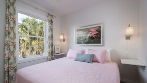 Quarto com cama grande, cortinas florais, quadro na parede e abajures.