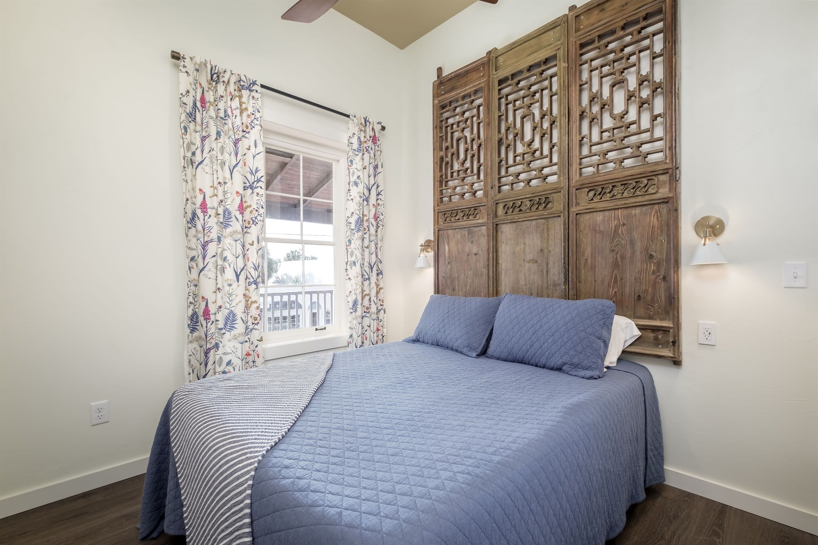 A bedroom with a bed, floral curtains, a wooden partition, and a window with a view.