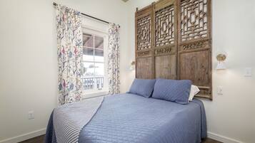 A bedroom with a bed, floral curtains, a wooden partition, and a window with a view.
