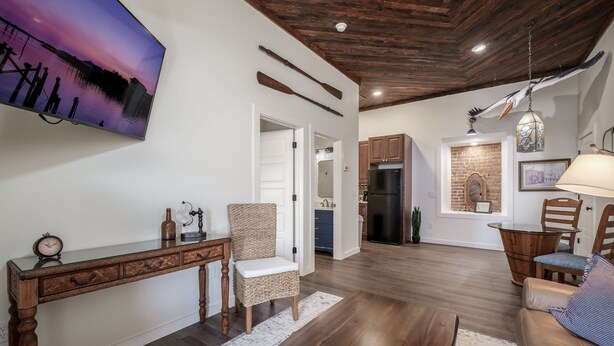 A spacious living area with a wooden floor, a dining table, a wicker chair, and a sofa. - Ship Style Luxury Downtown, Boat Trailer Parking! (Cedar Key)