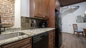 A kitchen with wooden cabinets, a granite countertop, a dishwasher, and a refrigerator. - Ship Style Luxury Downtown, Boat Trailer Parking! (Cedar Key)