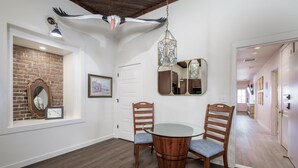 A dining area with a round table and chairs, a hanging light fixture, a mirror, and a brick wall. - Ship Style Luxury Downtown, Boat Trailer Parking! (Cedar Key)
