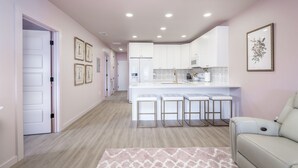 Una cocina moderna con armarios blancos, una isla central con taburetes e iluminación empotrada en el techo.