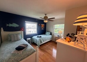 A bedroom with two beds, a ceiling fan, and a desk with a lamp.