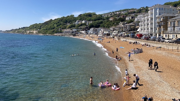 A beach with clear water, people, and buildings in the background.