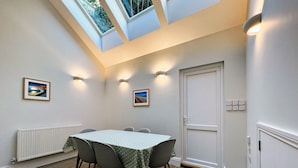A conference room with a high ceiling, skylights, a white door, and two framed pictures on the walls.