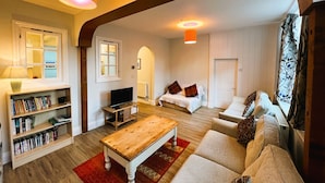 A cozy living room with a wooden coffee table, a bookshelf, a TV, and a sofa with patterned cushions.