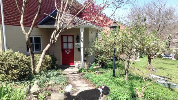 Uma casa com porta vermelha, caixa de correio e um jardim com um cão.