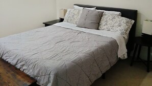 Quarto com cama, mesa de cabeceira, abajur e um quadro na parede.