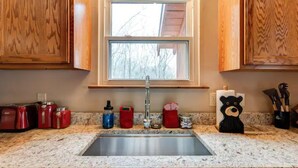 A kitchen with wooden cabinets, a granite countertop, a stainless steel sink, and various kitchen items. - Cupid's Haven: Private Cabin Close To All (Sevierville)