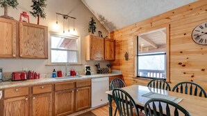 A wooden cabin interior with a kitchen and dining area, featuring wooden cabinets, a dining table with chairs, and a clock on the wall. - Cupid's Haven: Private Cabin Close To All (Sevierville)
