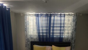 A bedroom with a bed, pillows, a rug, a nightstand, and a vase. - Cozy Home w/ private parking- 10 min to beach (Arecibo)