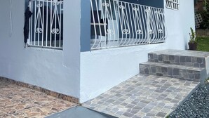 A residential building with a blue facade, numbered 348, featuring a balcony with decorative metal railings and a potted plant. - Cozy Home w/ private parking- 10 min to beach (Arecibo)