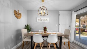A dining area with a wooden table, white chairs, a hanging light fixture, and a framed picture on the wall. - 4-bedroom vacation home just 4 minutes to Ohio State University (Columbus)