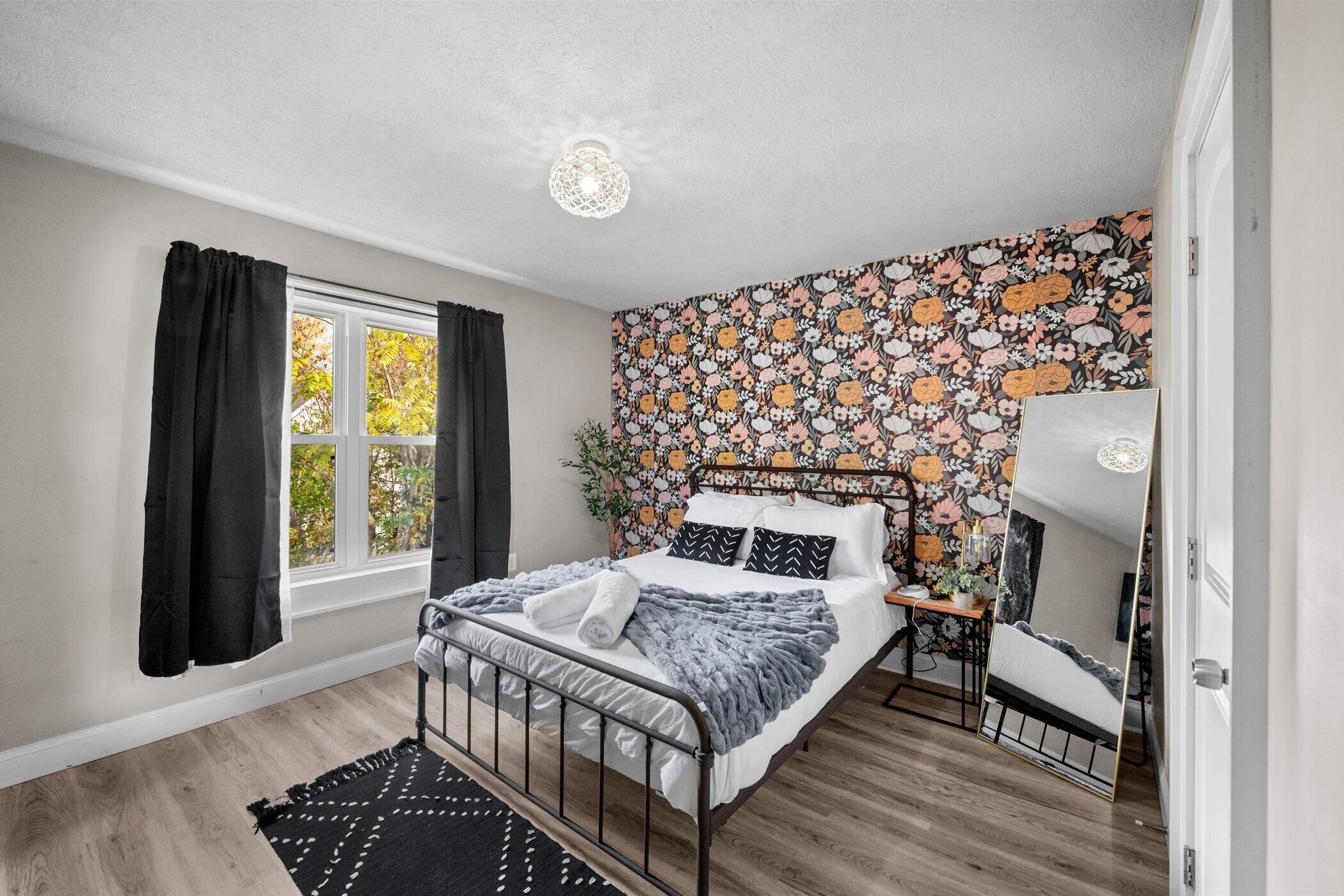 A bedroom with a bed, a bedside table, a mirror, and a window with curtains.