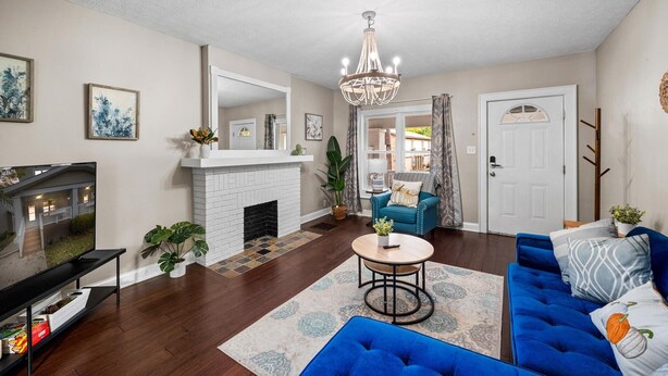 A living room with a fireplace, a blue sofa, a TV, and a chandelier. - Stylish 5BRs Next to Expo Center & Near Stadium,2 Free parking (Columbus)
