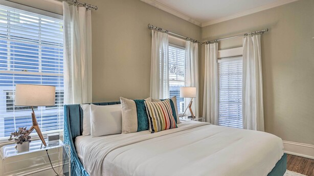 A bedroom with a large bed, two bedside lamps, a nightstand with a lamp, and a window with curtains. - Bright Apartment 3 Mi to Downtown Birmingham! (Birmingham)