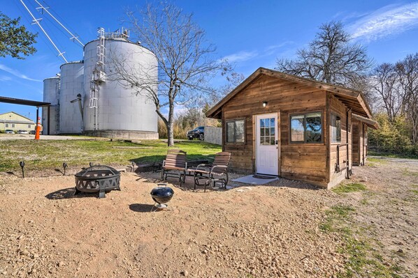 A rustic cabin with a wooden exterior, a small porch, and a gravel yard with outdoor seating.