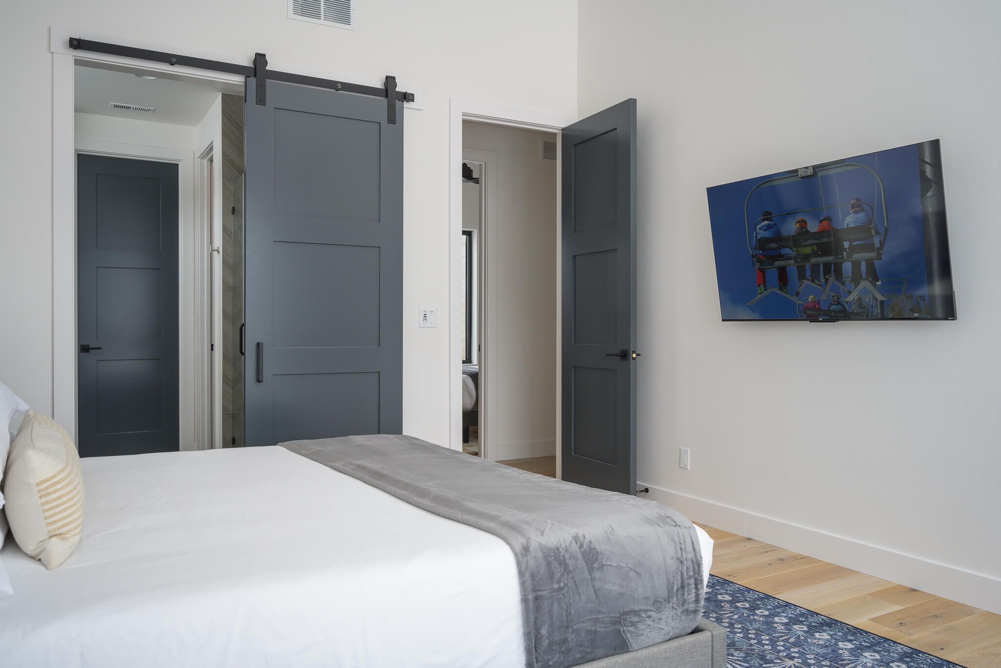 A bedroom with a bed, a gray sliding door, a painting of a ski lift, and a wooden floor.
