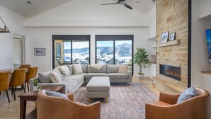 A spacious living room with a large sectional sofa, a fireplace, and a view of a mountainous landscape through large windows. - Wildhorse Summit | Private Gondola | Hot Tub, Pool, & Mountain Views (Steamboat Springs)