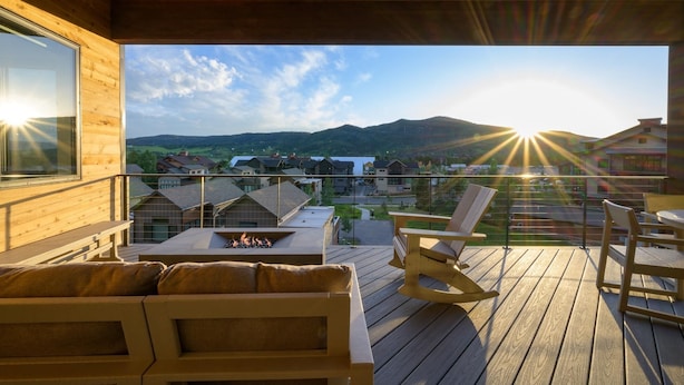 A wooden deck with a fire pit, outdoor seating, and a view of a residential area with mountains in the background. - Wildhorse Summit | Private Gondola | Hot Tub, Pool, & Mountain Views (Steamboat Springs)