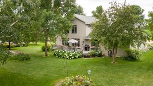 A two-story house with a covered patio, surrounded by well-maintained lawns and flowering plants.