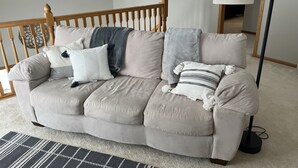 A beige sectional sofa with multiple pillows and a throw blanket, a wooden railing, a floor lamp, and a patterned rug.