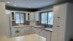 A kitchen with white cabinets, a wooden countertop, and a window with a view of trees.