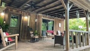 A wooden porch with a ceiling fan, rocking chairs, and a table with chairs. - Rustic cabin just outside of Madison! (Madison)