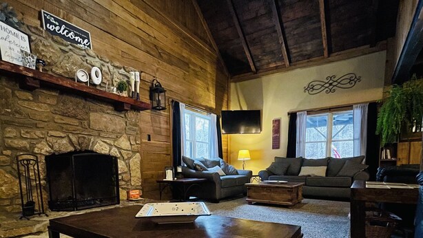 A cozy living room with a fireplace, wooden walls, and a comfortable seating area. - Rustic cabin just outside of Madison! (Madison)