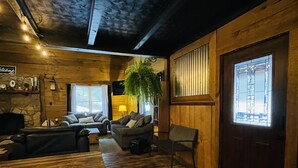 A cozy cabin interior with a wooden floor, a sofa, a chair, and a large window. - Rustic cabin just outside of Madison! (Madison)