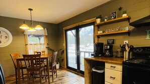 A kitchen with wooden flooring, a dining area with chairs, a coffee machine, and a stove. - Rustic cabin just outside of Madison! (Madison)