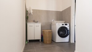 Ein Waschbereich mit Waschmaschine, Schrank und Mülleimer.