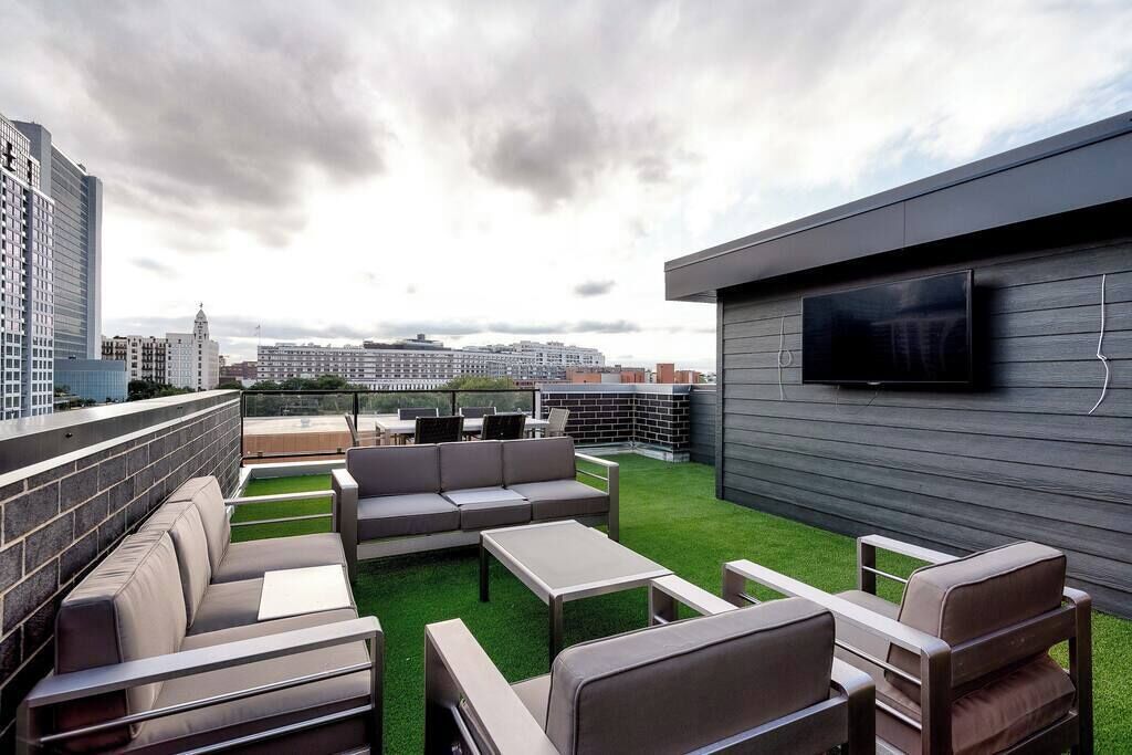 An outdoor seating area with a flat-screen TV, a sofa, and a table, overlooking a cityscape.