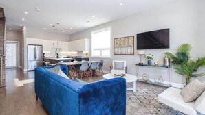 Een moderne woonkamer met een blauwe bank, een witte fauteuil, en een eethoek met een tafel en stoelen.