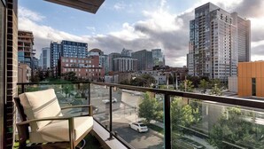 Een balkon met een stoel, een glazen hekwerk en uitzicht op een stadsbeeld met hoge gebouwen.