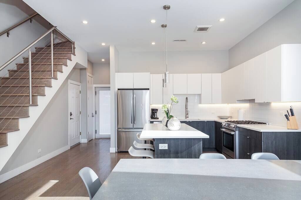 A modern kitchen with a central island, stainless steel appliances, and a staircase with wooden steps.