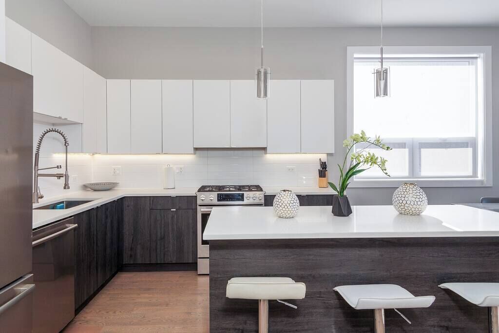Een moderne keuken met witte kasten, een centraal kookeiland met krukken, een fornuis en hanglampen.