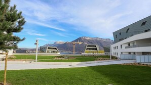 A modern building with a flat roof and a large glass facade, surrounded by a well-maintained lawn and a mountain in the background. - The nest of Lake Annecy (Annecy)