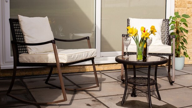 A patio area with two rocking chairs, a small round table with a vase of flowers, and a potted plant.
