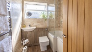 A bathroom with a wooden vanity, a white toilet, a glass shower enclosure, and a window with a view of greenery outside.