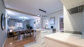 Uma cozinha moderna com uma ilha central, uma área de refeições com cadeiras, um sofá e uma pequena mesa com abajur.