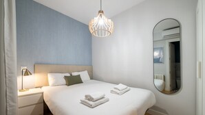 Quarto moderno com uma cama grande, mesa de cabeceira com abajur, espelho redondo e luminária pendente.