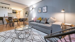 Uma sala de estar moderna com um sofá cinzento, uma mesa de centro de vidro e um espaço de jantar com cadeiras e uma mesa.